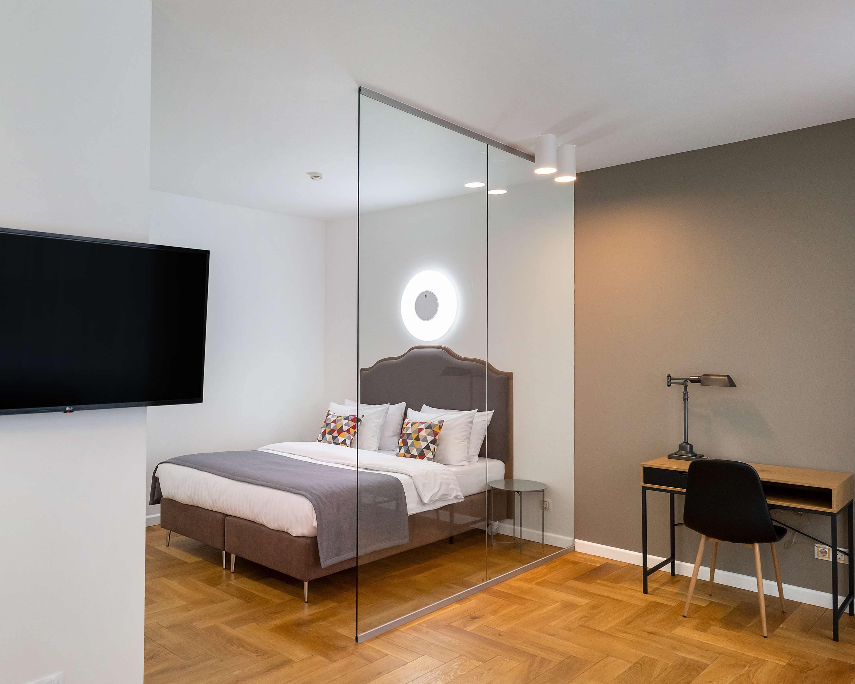 A modern bedroom with a bed, a desk, a chair, and a TV mounted on the wall.