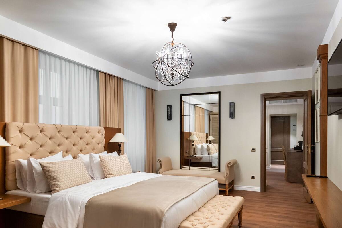 A spacious bedroom with a large bed, a bench, a mirror, and a chandelier.
