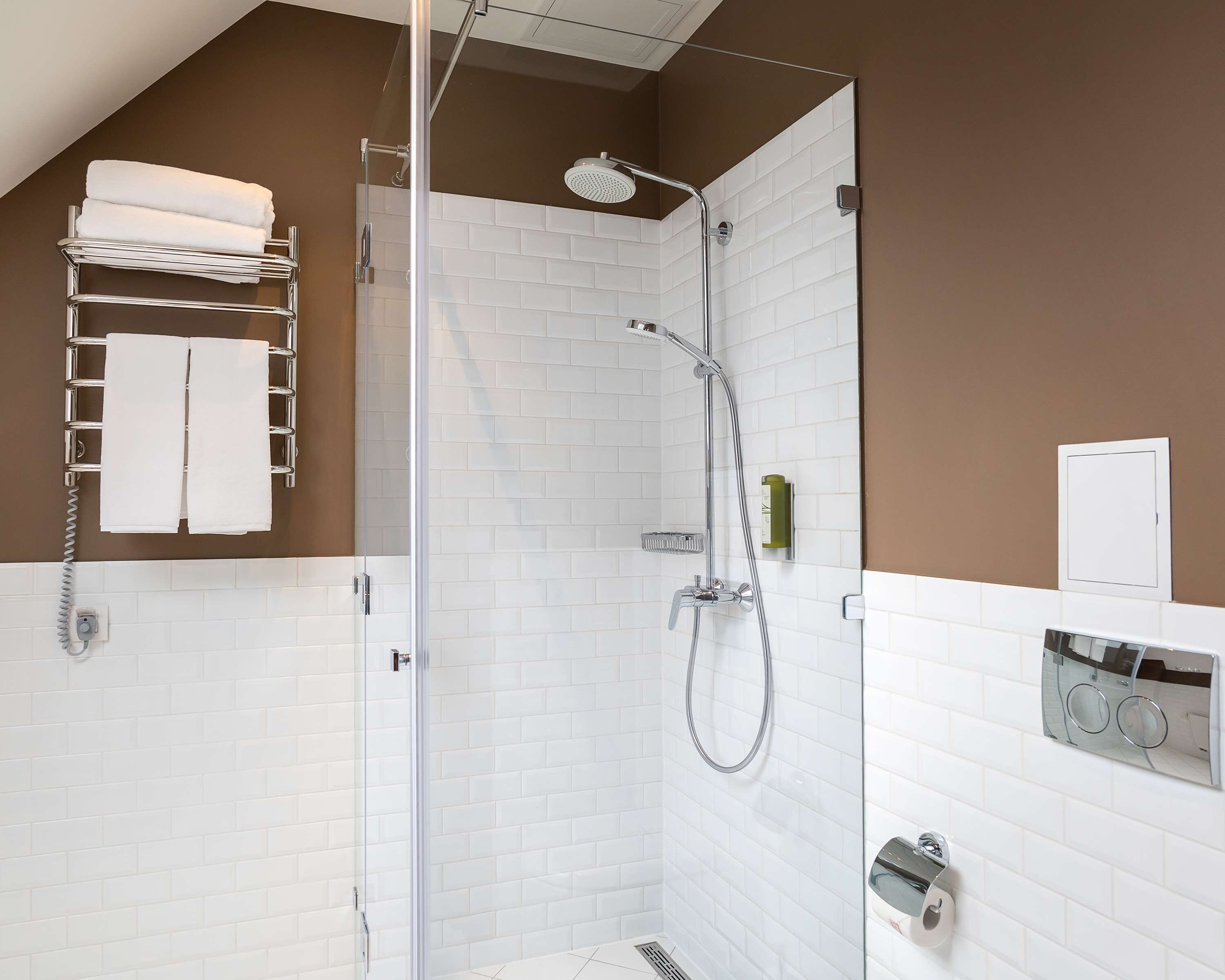A modern shower area with a glass door, white tiled walls, and a towel rack with two towels.