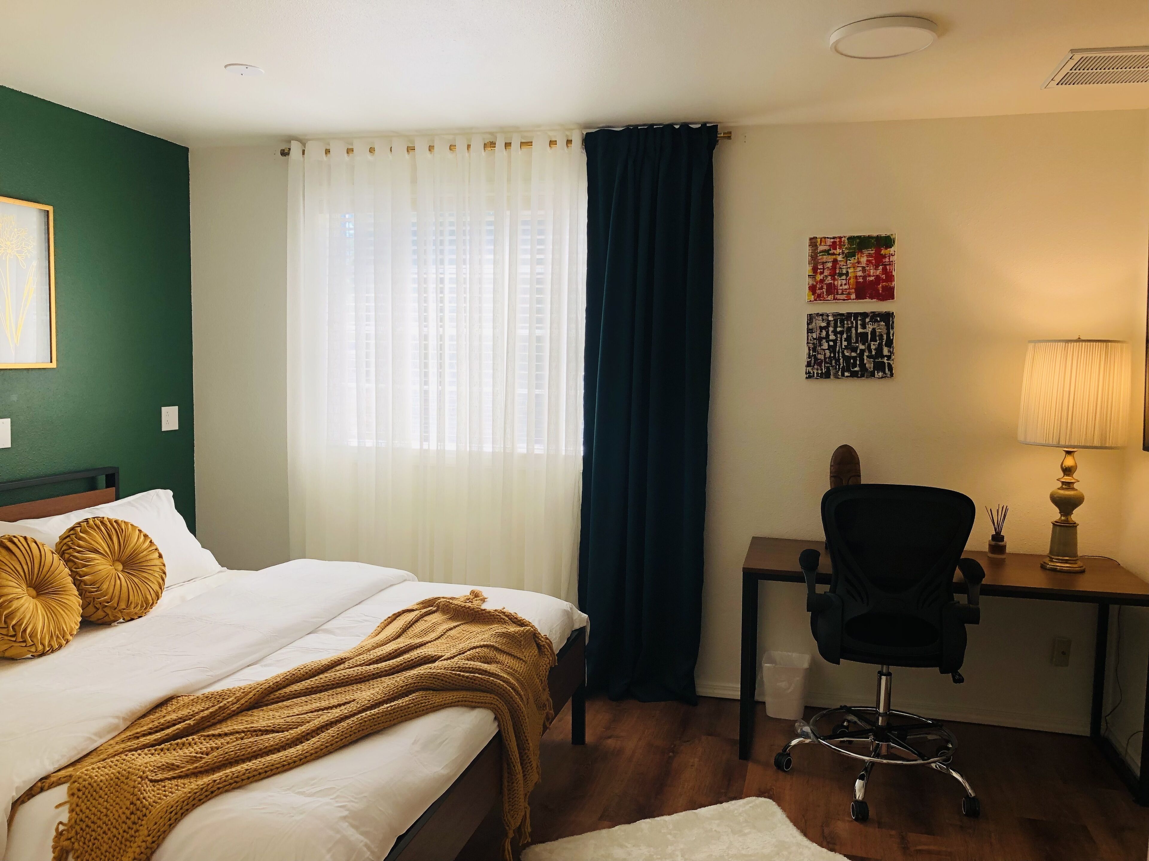 A hotel room with a bed, a desk, a chair, a lamp, and a window with curtains.
