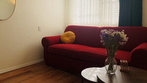 En röd soffa med en gul kudde, en genomskinlig vas med blommor och ett litet träbord.