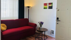 Ett rum med en röd soffa, ett litet runt bord med en vas med blommor, en golvlampa och en dörr med ett handtag.