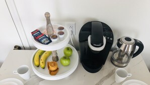 En köksbänk med en kaffebryggare, en vattenkokare, en tallrik med bananer och äpplen, en servett och en kopp.