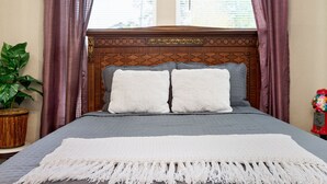 Un letto ben rifatto con copriletto grigio e cuscini bianchi, una coperta bianca e una testiera decorativa.