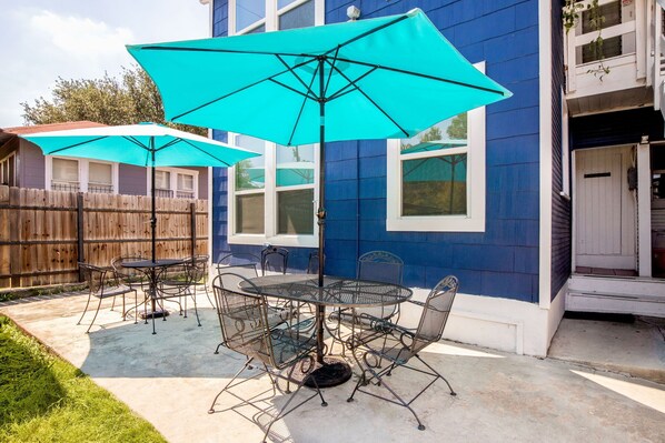 Relax under the shade of a large umbrella on this outdoor patio, adjacent to a charming building with an entrance.