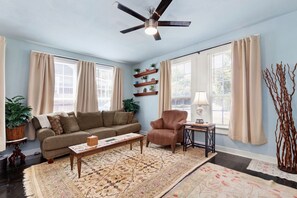 Relax in this inviting living room with a sofa, armchair, and table, surrounded by decorative items and a large window.