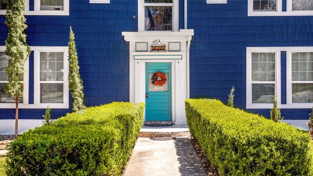 Una casa a due piani con facciata blu, rifiniture bianche e una porta verde.