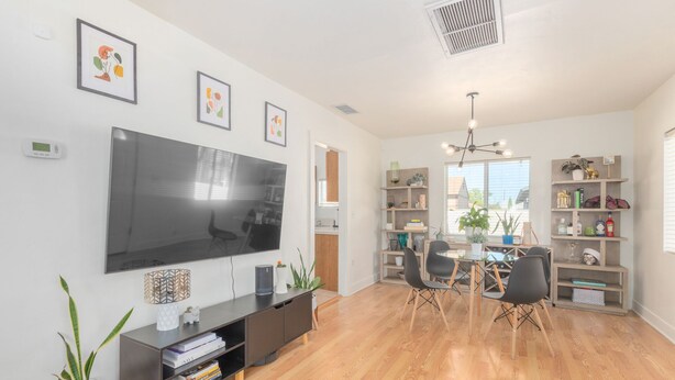 A modern living room with a flat-screen TV, wooden flooring, a dining area with a table and chairs, and a bookshelf filled with books and decorative items. - Charming Bungalow In The Heart Of Downtown Phoenix (Phoenix)