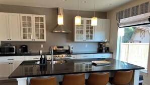 A modern kitchen with white cabinets, a large island with bar stools, stainless steel appliances, and pendant lighting. - Modern home in downtown Sumner, WA, 34 mi from Lumen Field (Sumner)