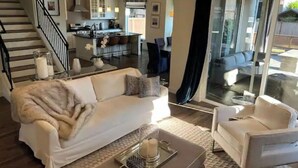 A modern living room with a sofa, armchair, and coffee table. A kitchen is visible in the background, and a staircase leads to another level. - Modern home in downtown Sumner, WA, 34 mi from Lumen Field (Sumner)
