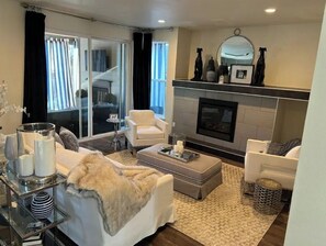 A modern living room with a fireplace, white sofas, a coffee table, and a glass coffee table with decorative items.