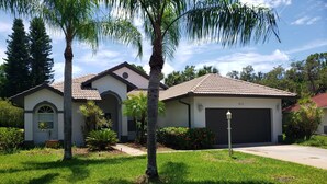 A residential house with a tiled roof, a garage, and a well-maintained lawn with palm trees. - Cheerful 3 bedroom home with pool -- 5 min from beach! (Nokomis)