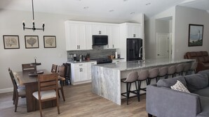 A modern kitchen with white cabinets, a black refrigerator, and a central island with bar stools. - Cheerful 3 bedroom home with pool -- 5 min from beach! (Nokomis)