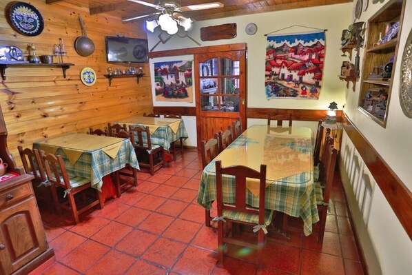 Un comedor con paredes de madera, suelo de baldosas rojas y mesas cubiertas con manteles a cuadros.