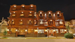 A multi-story wooden building with balconies and illuminated windows, likely a hotel or guesthouse. - Hotel Sirenuse (Mar del Plata)