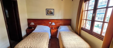 A room with two beds, wooden headboards, a ceiling fan, and a window with a view of buildings.