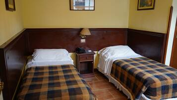 Una habitación con dos camas, cada una con una colcha a cuadros, una mesita de noche con lámpara y un reloj de pared.
