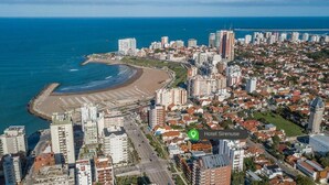 An aerial view of a coastal city with a prominent beach, Hotel Sirenuse, and surrounding high-rise buildings. - Hotel Sirenuse (Mar del Plata)