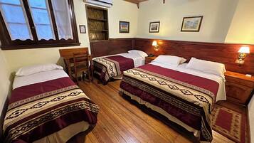 A hotel room with three beds, wooden flooring, a wooden ceiling, and a window with curtains.