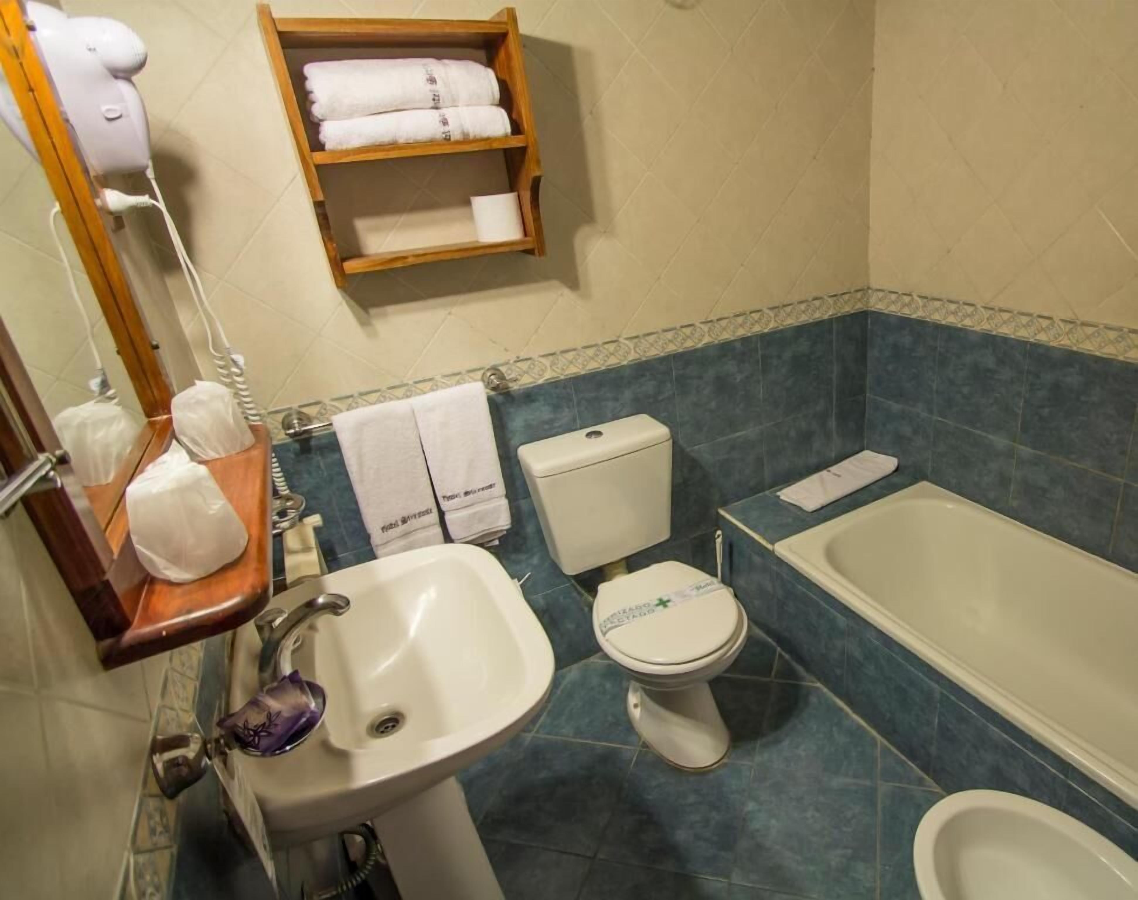 A bathroom with a sink, toilet, and bathtub. There is a towel rack with towels and a soap dispenser.
