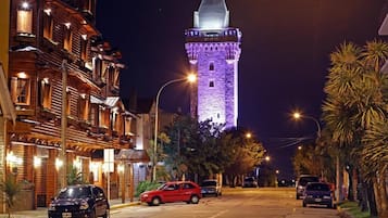Eine Straße mit einem in Lila beleuchteten Turm, parkenden Autos und Häusern mit Balkonen.