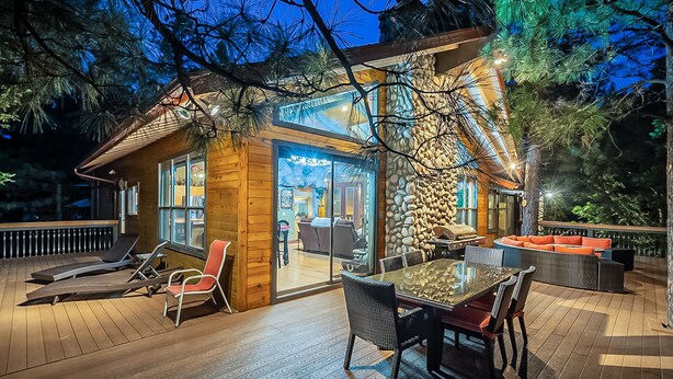 A wooden deck with a glass-enclosed dining area, outdoor seating, and a stone wall. - Custom 6 Bedroom 4 full bathrooms Cabin with Amazing hillside Views, fenced lot. (Pinetop-Lakeside)