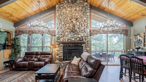 A spacious living room with a stone fireplace, leather sofas, and a dining area with a view of the outdoors. - Custom 6 Bedroom 4 full bathrooms Cabin with Amazing hillside Views, fenced lot. (Pinetop-Lakeside)