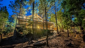 A multi-story wooden cabin with a balcony, surrounded by dense forest. - Custom 6 Bedroom 4 full bathrooms Cabin with Amazing hillside Views, fenced lot. (Pinetop-Lakeside)