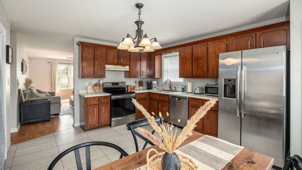 A modern kitchen with wooden cabinets, stainless steel appliances, and a dining area with a table and chairs. - Wild Joy| King Bed, Pet-Friendly Stay, Fenced Yard (Clarksville)
