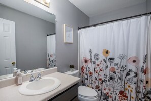 Ein Badezimmer mit weißem Waschbecken, Toilette und einer Duschkabine mit Blumenmuster.