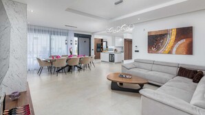 Una sala moderna con un sofá, un comedor con sillas y una mesa, y una cocina al fondo.