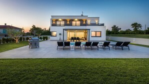 Una casa moderna de dos pisos con un patio que cuenta con mobiliario exterior y una parrilla.