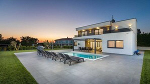 Una casa moderna de dos pisos con piscina, mobiliario exterior y césped cuidado.