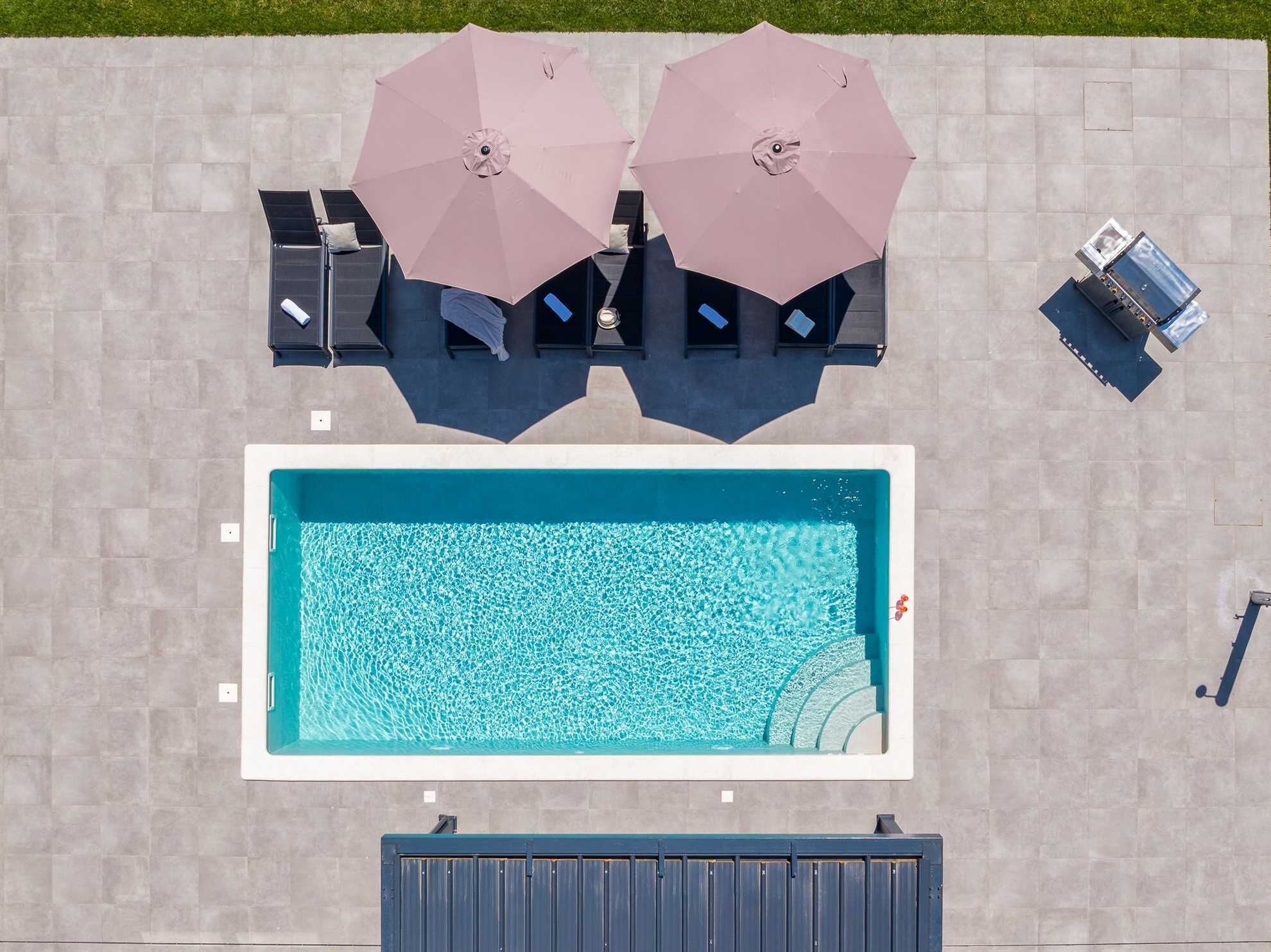 An aerial view of a swimming pool with two umbrellas, lounge chairs, and a water filtration system.