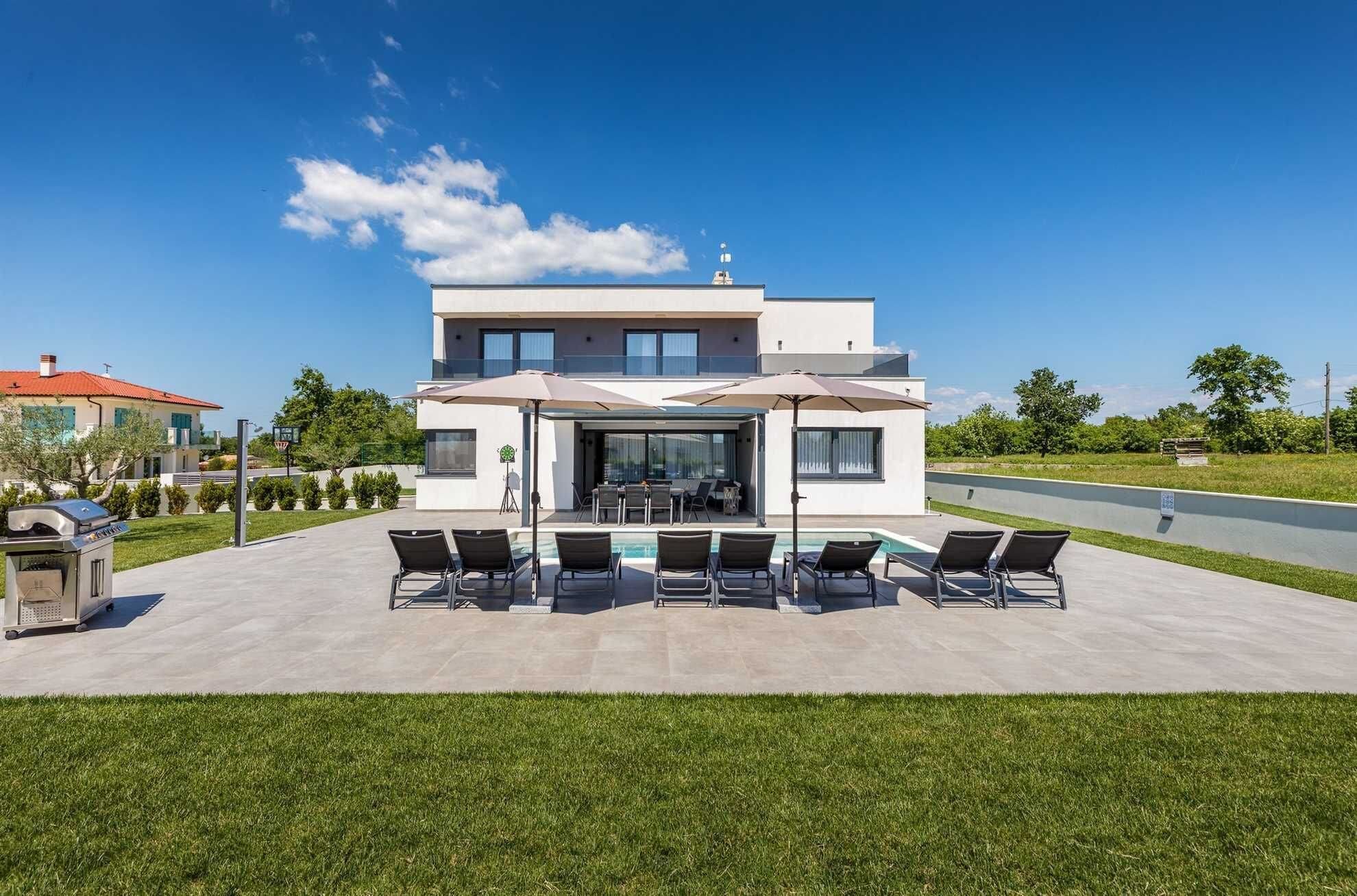 Una casa moderna de dos pisos con un patio que cuenta con una piscina y sillones de descanso.