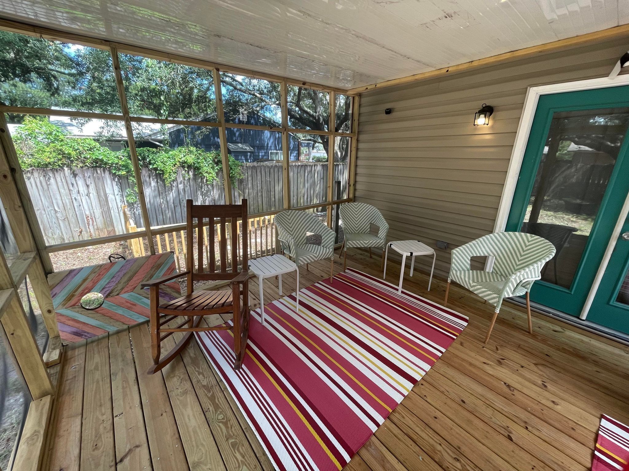 Une véranda couverte avec un plancher en bois, des tapis à rayures et du mobilier d’extérieur comprenant des chaises et une petite table.