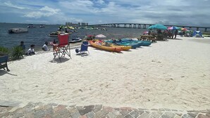 A beach with kayaks, a pier in the background, and a paved walkway. - New! GREEN HOUSE minutes from Navarre beach and restaurants (Navarre)