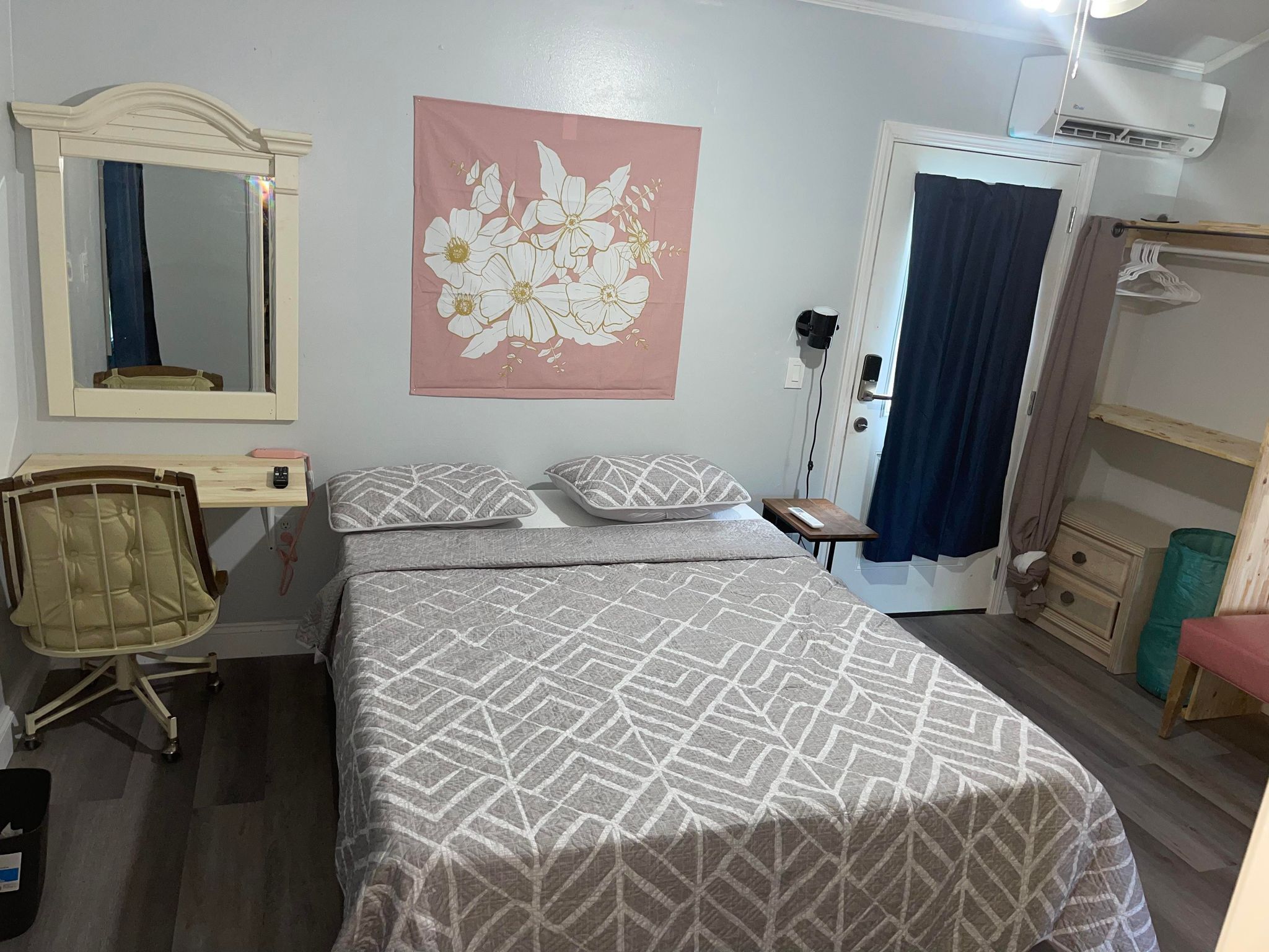 Une chambre à coucher comprenant un lit, une chaise, une table de chevet, un miroir, une armoire et un mur orné d’un tableau représentant des motifs floraux.