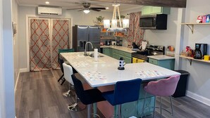 A modern kitchen with a central island, bar stools, a ceiling fan, and a microwave. - New! GREEN HOUSE minutes from Navarre beach and restaurants (Navarre)