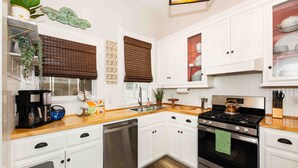 Une cuisine moderne avec des meubles blancs, un lave-vaisselle en acier inoxydable, une cuisinière à gaz et un plan de travail en bois.
