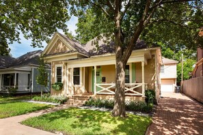 A single-story house with a front porch, a small front yard, and a garage. - Boho Bungalow In Houston Heights (Houston)