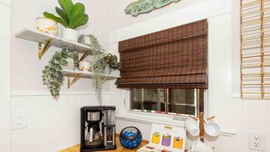Une cuisine équipée d’une machine à café, d’un panier de collations et d’une fenêtre avec des stores.