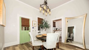 Un coin repas avec une table ronde, des chaises à revêtement blanc, une porte verte, un miroir et un lustre.