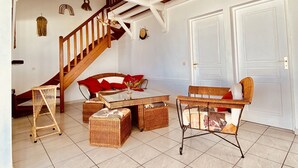 Un ampio soggiorno con soffitto alto, travi in legno, una scala, mobili in vimini e pavimento piastrellato.