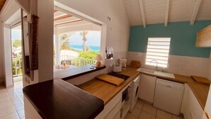 Una cucina con piano di lavoro in legno, mobili bianchi, lavastoviglie e vista sull'oceano.