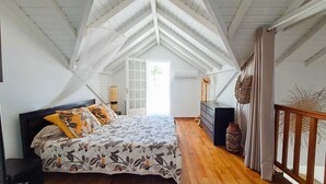Una camera da letto con soffitto spiovente, un letto con biancheria da letto floreale, un comò e vista sull'esterno.