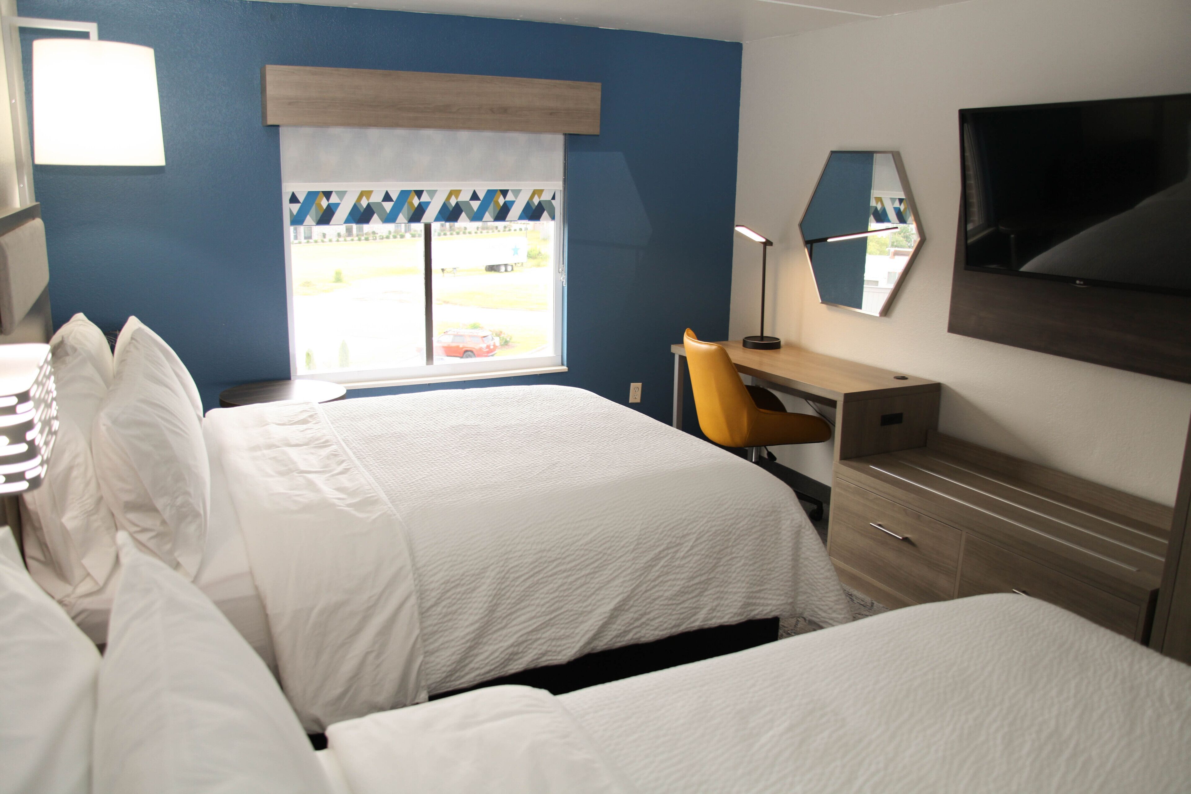A hotel room with two beds, a desk, a chair, a TV, and a window with a view of the outside.