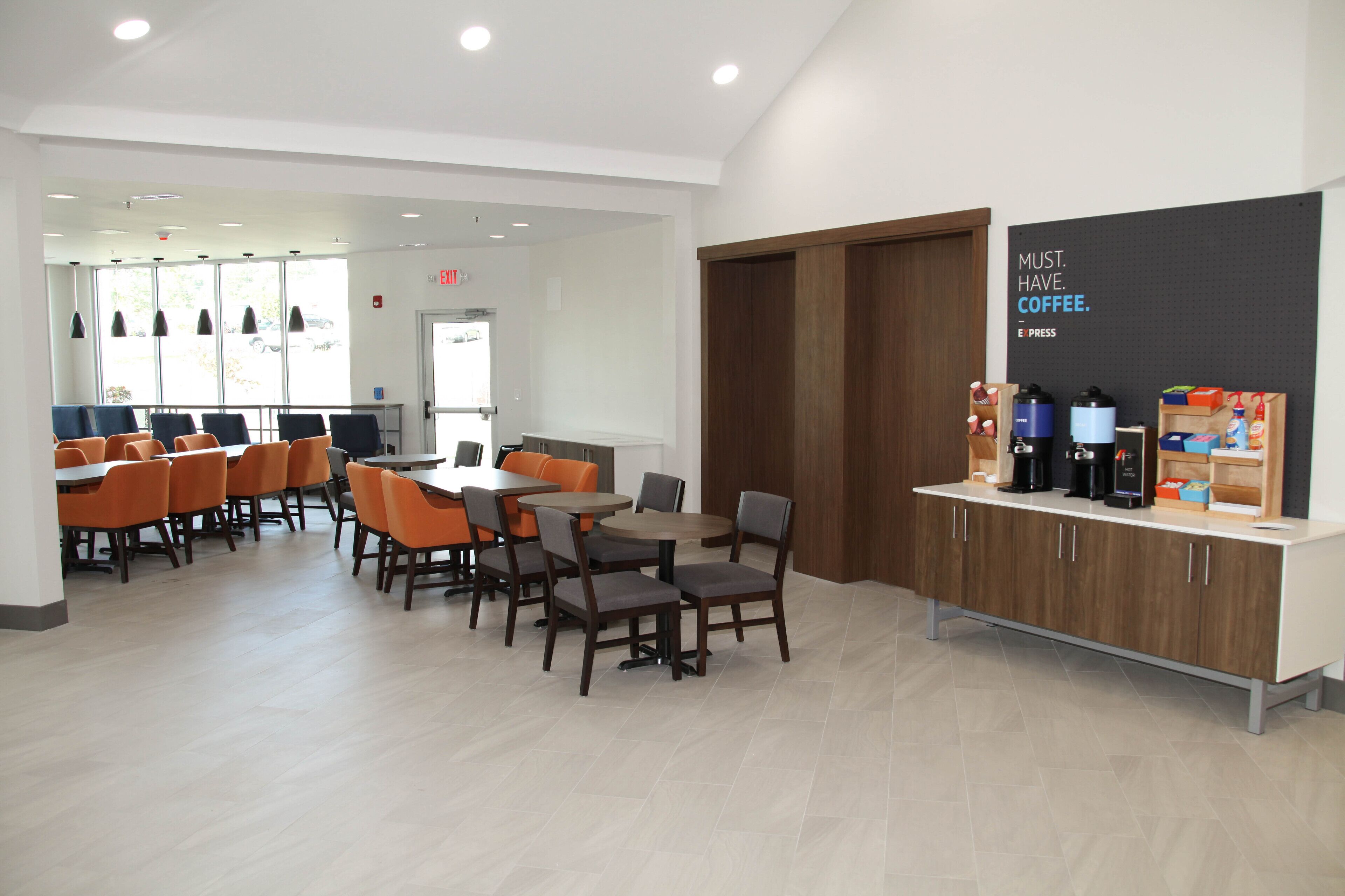 Un café moderne doté de plusieurs espaces de détente, comprenant des tables et des chaises, ainsi qu’un coin café équipé de divers appareils pour préparer le café.
