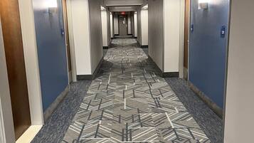 Un pasillo de hotel con alfombra estampada, puertas a ambos lados y techo con iluminación empotrada.