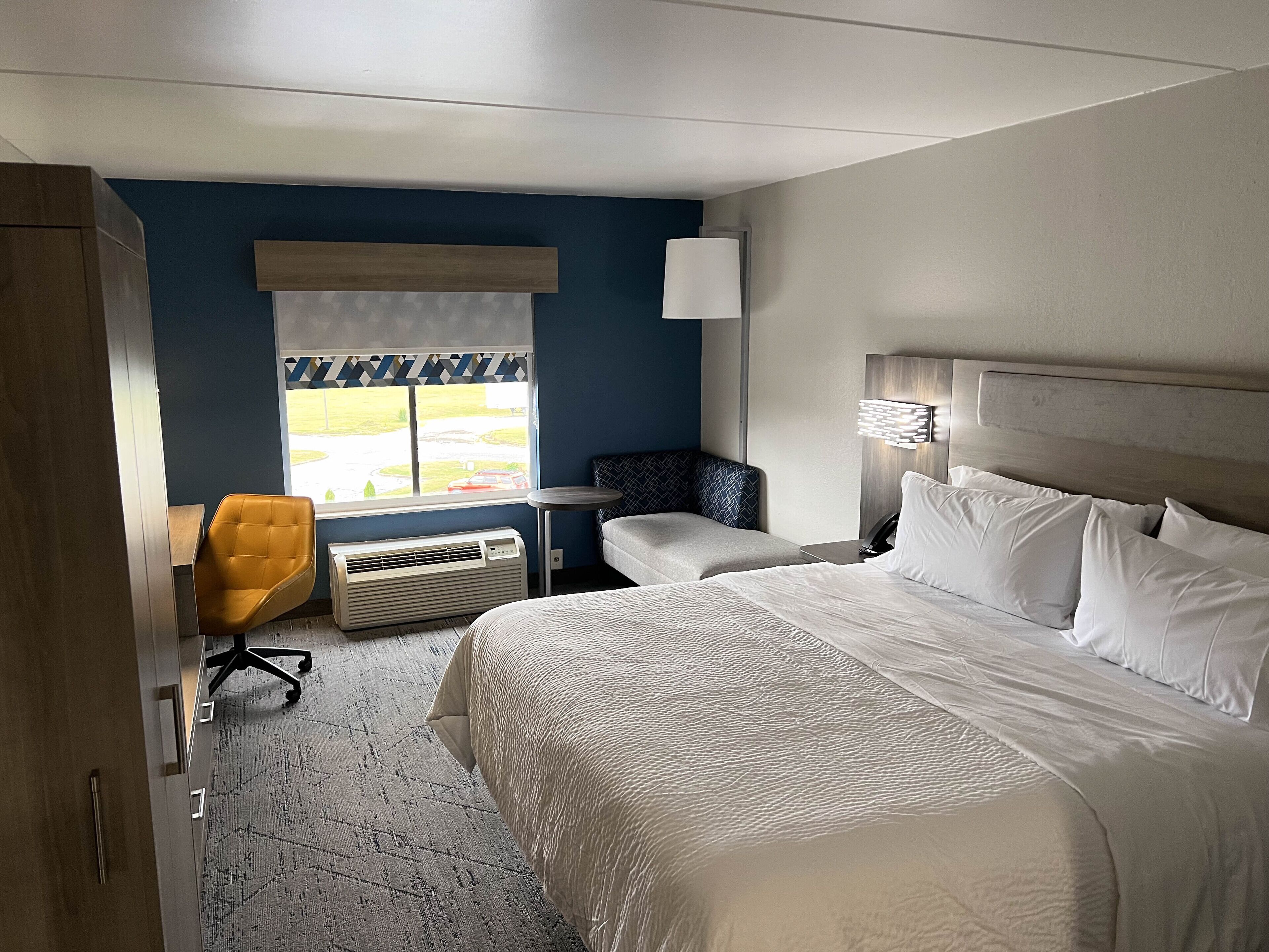 Ett hotellrum med en stor säng, ett skrivbord, en stol och ett fönster med utsikt över omgivningarna.